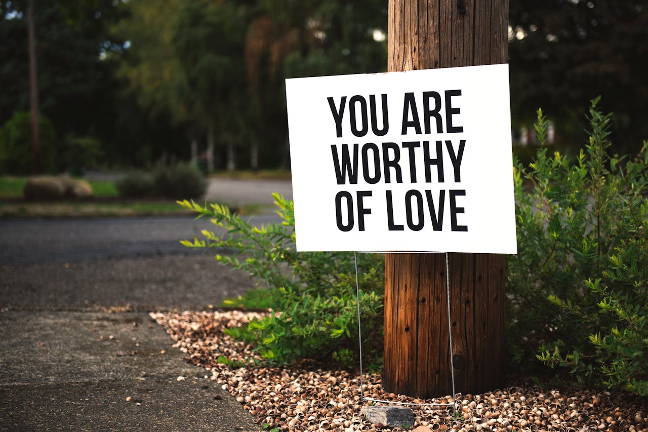 A positive message sign You are worthy of love in a park setting.